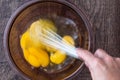 Raw eggs in glass bowl, womanÃ¢â¬â¢s hand with stainless steel whisk, whipping eggs, on a wood table